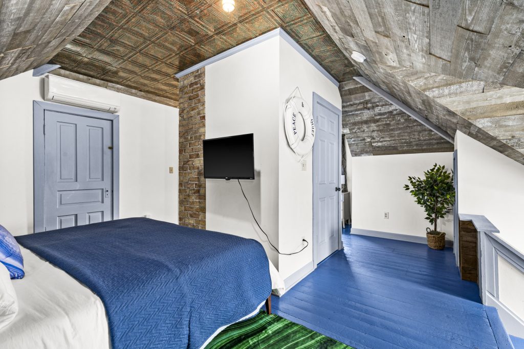 Third floor bedroom with a TV, brick accent, and open loft.